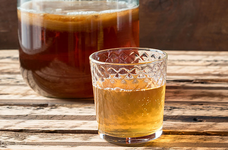 a glass of kombucha sits in front of a jar of homemade kombucha