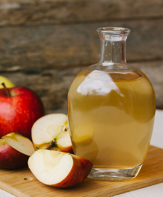 apple cider vinegar sits in a jar in front of apples