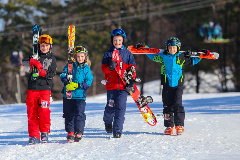 a group of four kids holding their ski gear and posing for photo