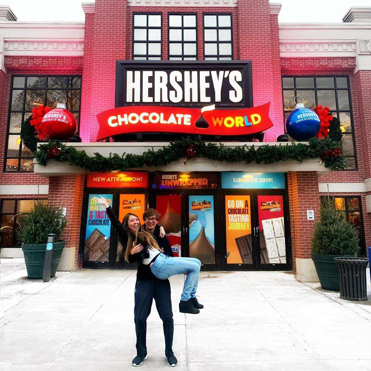 A guy picking up girl carrying in hands posing for a photo in front of hershey chocolate world
