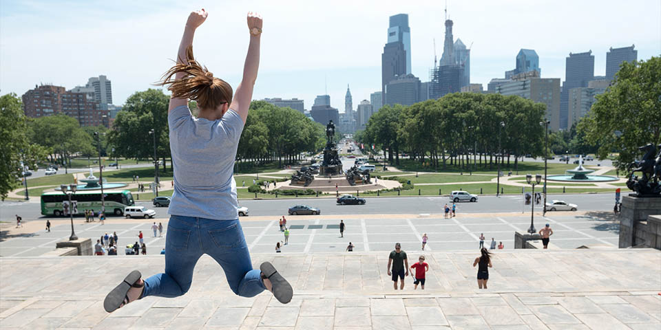 a women jumping posing for a photo Philly skyline in the back