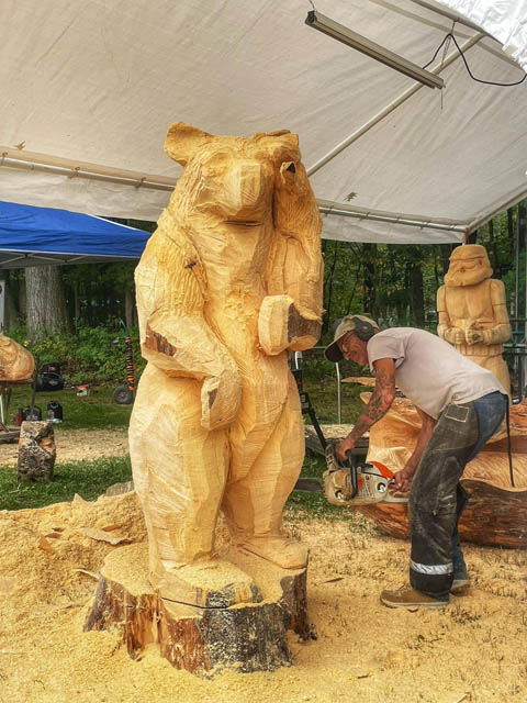 an artist carving a bear out of a wood log using chainsaw
