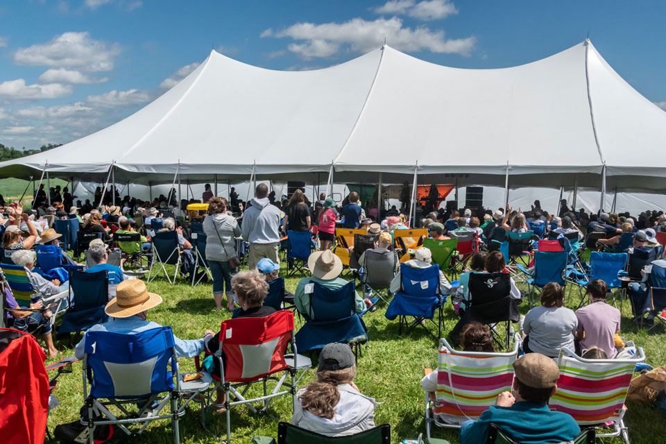 people sitting in folding chairs under and around a huge white tent