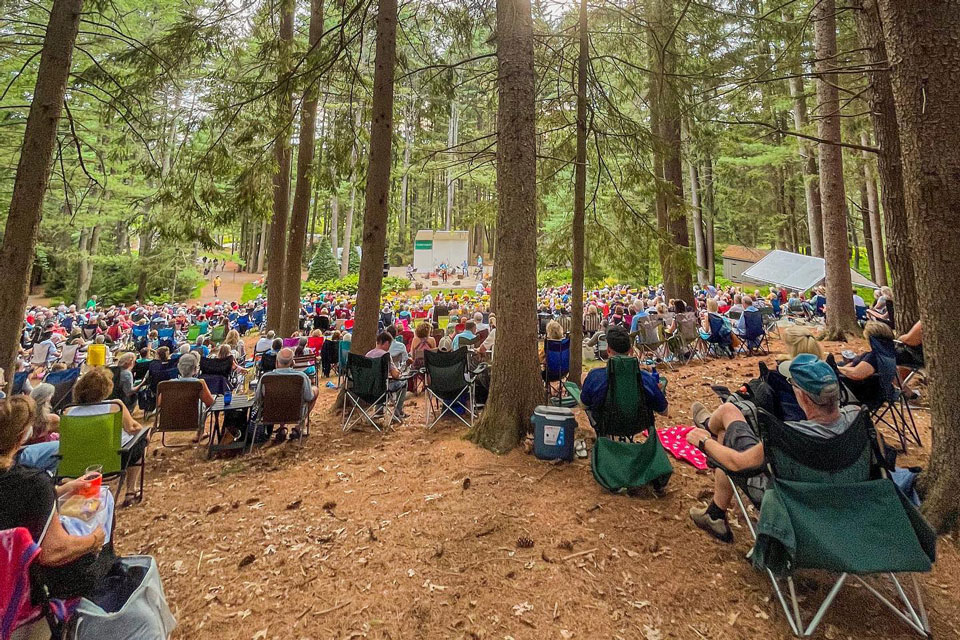 People sitting in the woods with camping chairs enjoying concert