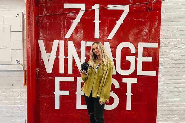 A girl with camera standing infront of fest signage board