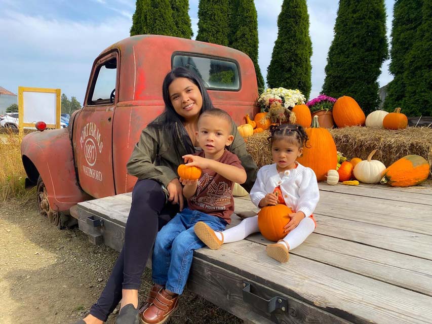 kids holding pumpkins in hands and sitting on pumpkin wagon along with their mother
