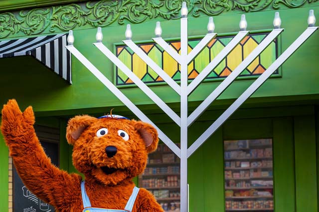 Sesame Place character posing for photo with hannukah lights