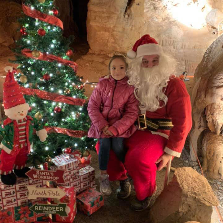 Little girl posing with Santa next to Christmas Tree in a Cave