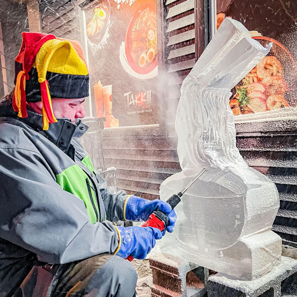 A person with cap on head carving a sculpture from ice