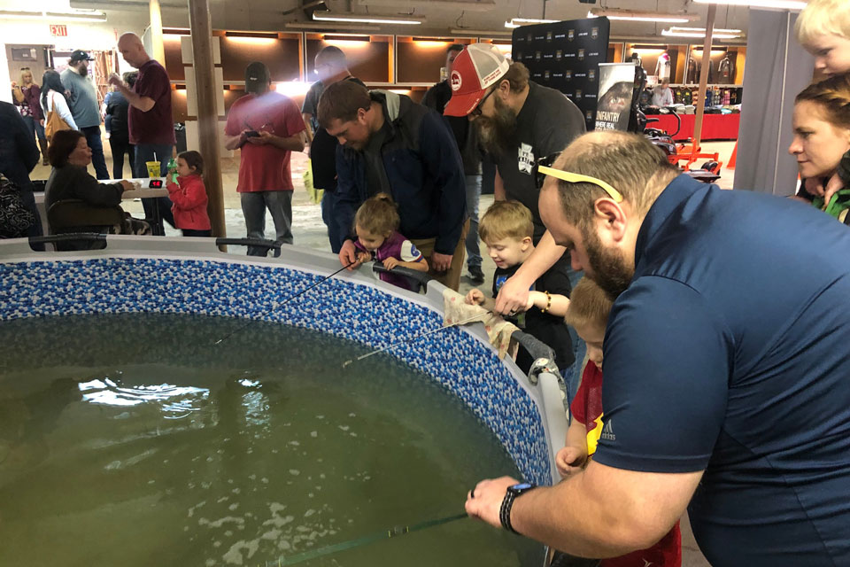 little kids trying fishing from a indoor pool with the help of their parents