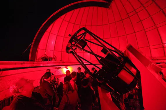 People inside an observatory look at a telescope under red lighting