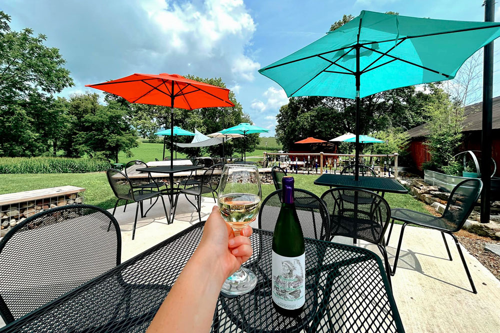 A person enjoying wine outdoor under colored umbrellas