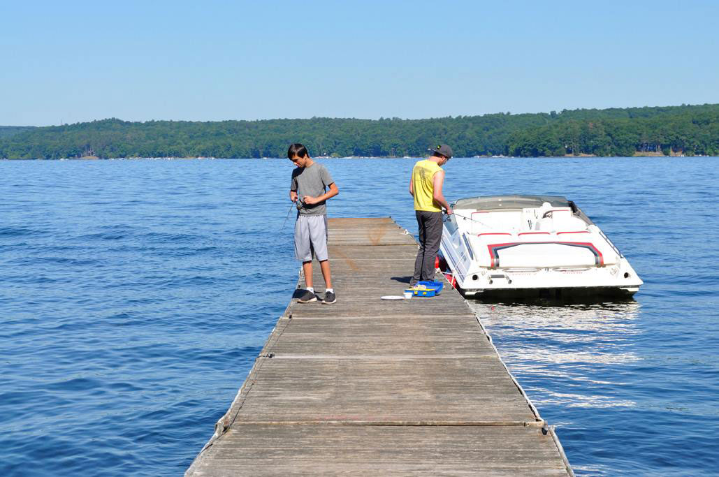two persons fishing from a dock and a boat docked on one end of the dock