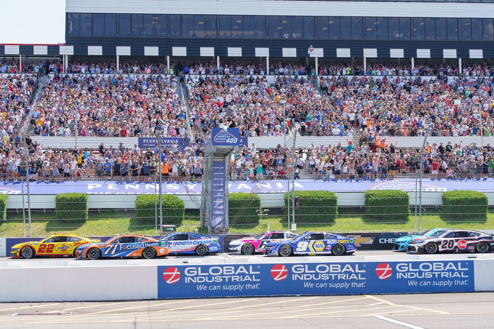 race cars speeding around a track, with a large crowd of fans filling the grandstands, capturing the excitement and energy of a motorsports event