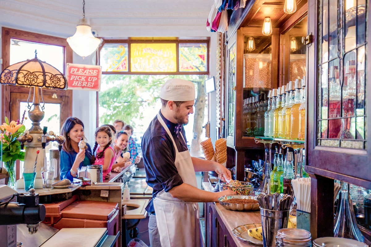 a server serving ice cream to patrons dressed with skull cap and chef apron