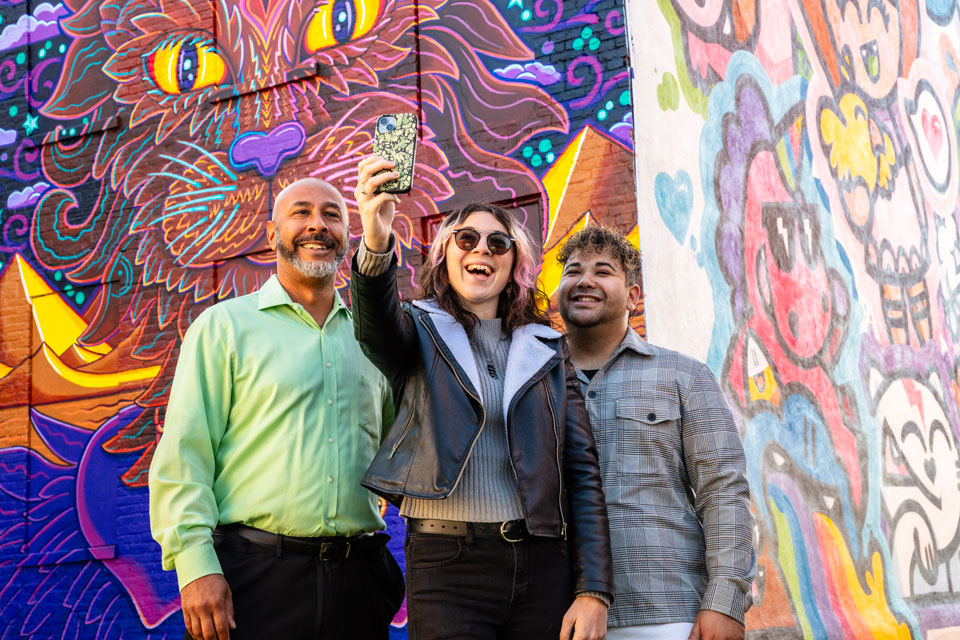 three friends taking a selfie in front of a street art mural