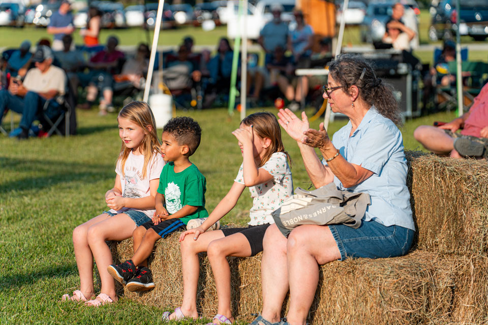 kids along with a women sitting on hay stack bales enjoying Bluegrass festival
