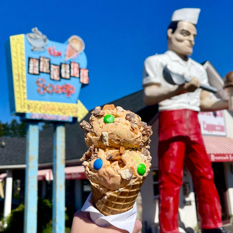 holding ice cream in waffle cone in front of a retro ice cream parlor with a Giant server statue holding scoop