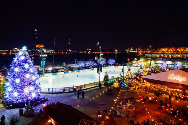 people skating on Ice rink by river, christmas tree and holiday lights around