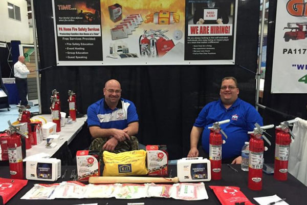 A couple of men sitting at a table with fire extinguishers and safety kits