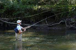 persona pescando de pie en la corriente del río Shenango