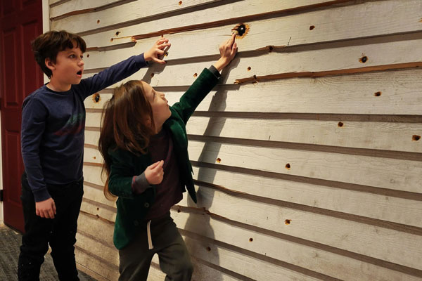kids pointing at bullet holes on wall