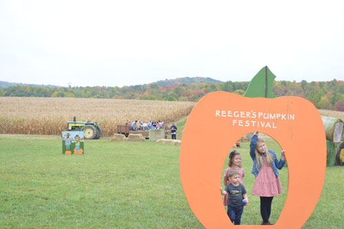 kids posing for photo using gaint pumpkin photo prop on farm