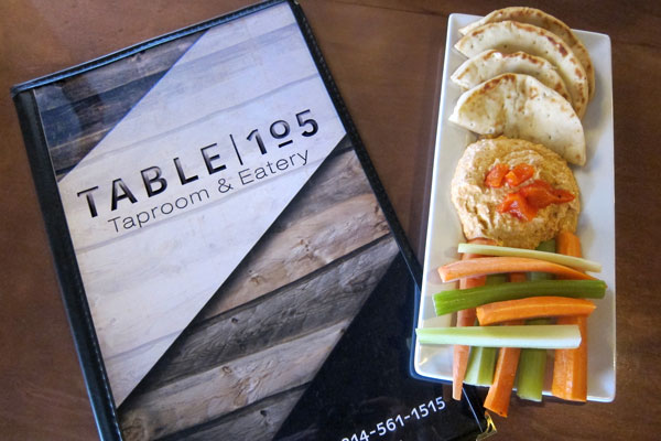 menu booklet on left a serving of pita bread with hummus carrot and celery on right placed on a table
