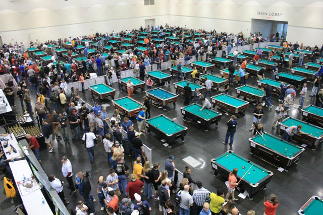 A large group of people in a large room with many poll tables