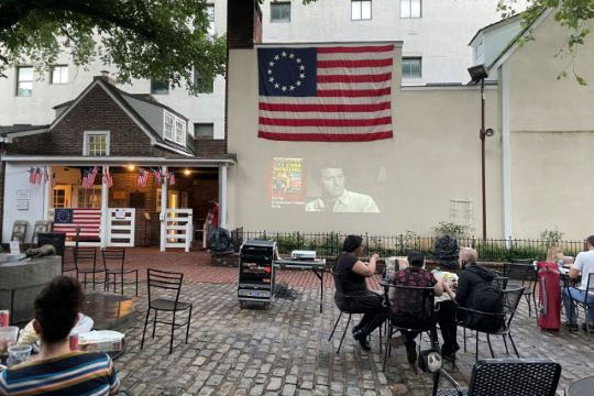 people watching movie project on wall outdoor below American flag