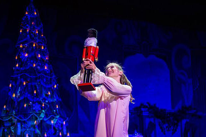 theater artist holding a prop toy while perform act, christmas tree in the back
