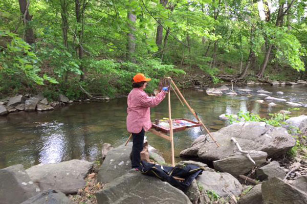 a women painting by creek standing on Boulders