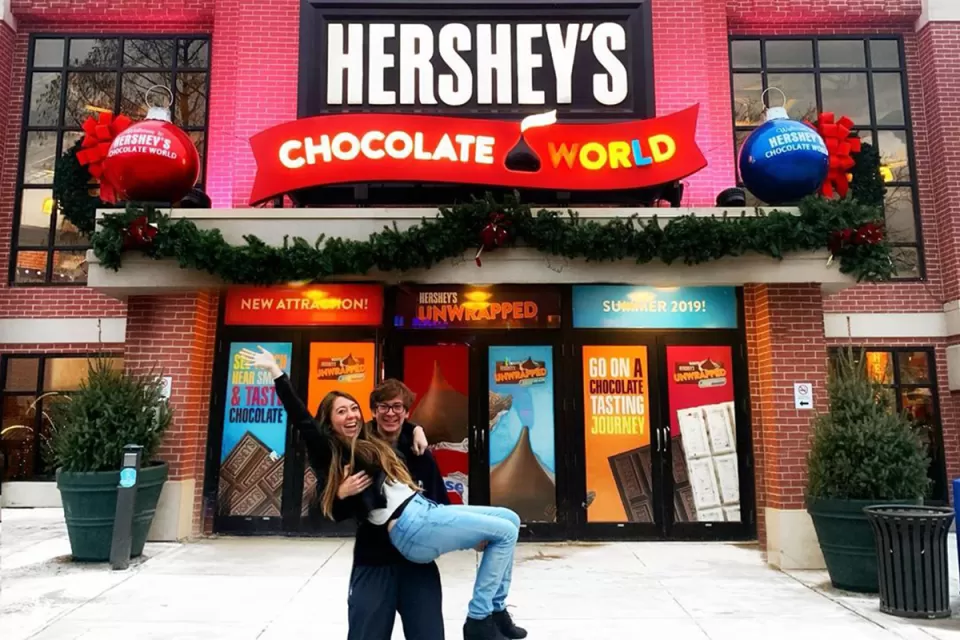 A guy picking up girl carrying in hands posing for a photo in front of hershey chocolate world