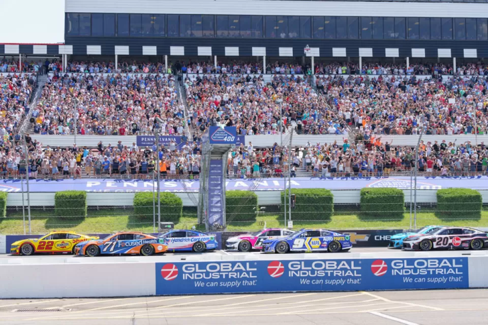 race cars speeding around a track, with a large crowd of fans filling the grandstands, capturing the excitement and energy of a motorsports event