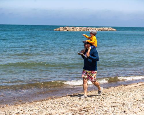 son hopping on father shoulder and walking on beach by lake