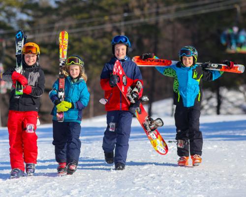 a group of four kids holding their ski gear and posing for photo