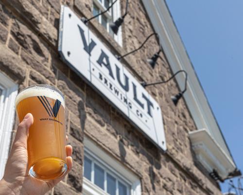 holding a beer glass in front of Vault Brewing Company signage board