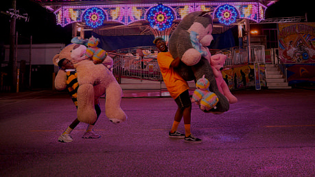 Two individuals carrying large stuffed animals at a fair