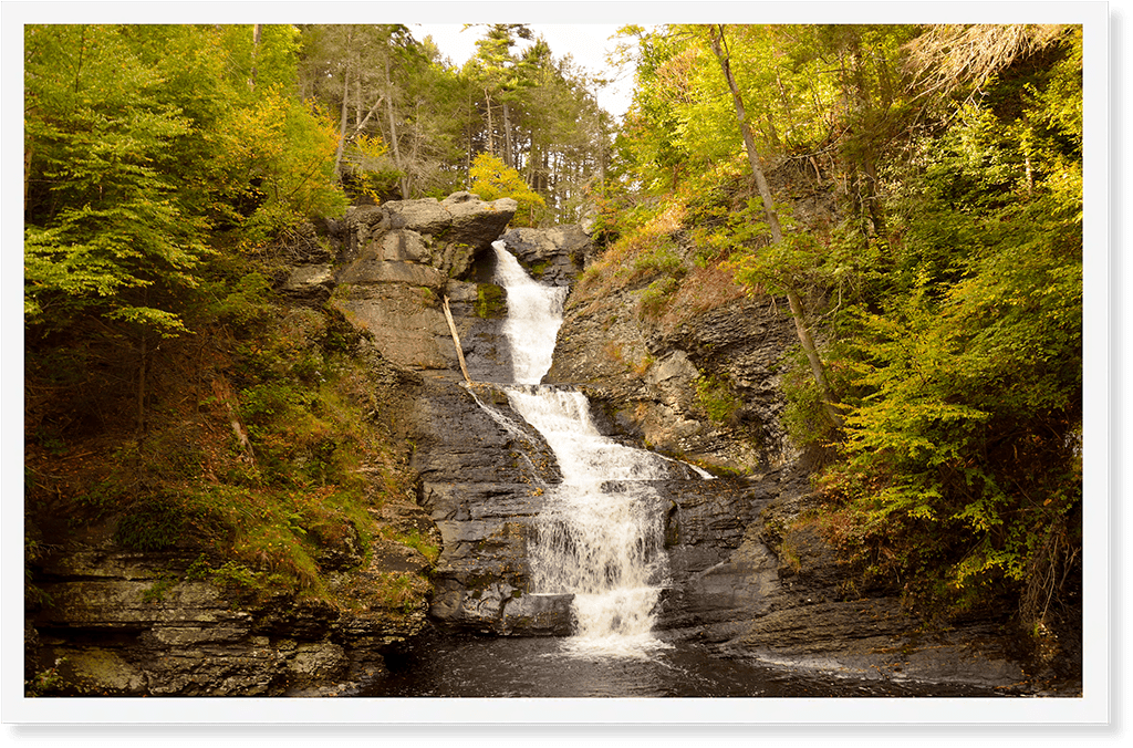 A waterfall flowing down rocks, surrounded by green trees and moss